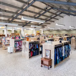 Ruim winkelvloer met kledingrekken, stellingen en winkelafdelingen in een kringloopwinkel