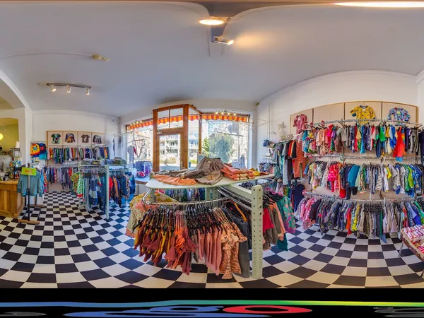 Ruime winkelruimte met zwart-wit tegelvloer, rekken vol gekleurde kinderkleding aan alle zijden en uitgestalde items in het m