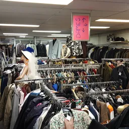 Overzicht van de winkelvloer met meerdere rekken vol tweedehands kleding, een roze uithangbord zichtbaar boven