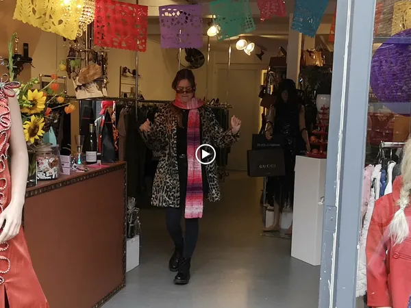 Binnenkant van kringloopwinkel met kledingrekken, decoraties en een bezoekers die kleding bekijkt