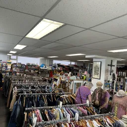 Winkelvloer van kringloopwinkel met kledingrekken, boekenkasten en shoppers die rondkijken
