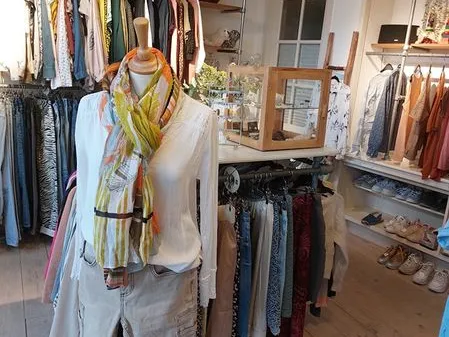 Winkelinterieur met kledingrekken, een etalagepop met geel-groen sjaaltje en diverse tweedehands kleding