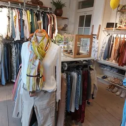Winkelinterieur met kledingrekken, een etalagepop met geel-groen sjaaltje en diverse tweedehands kleding