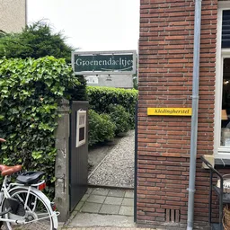 Voorgevel van kringloopwinkel met groene klimop, houten deur en naamborden 'Groenendaeltje' en 'Kledinghersel', fiets op voor