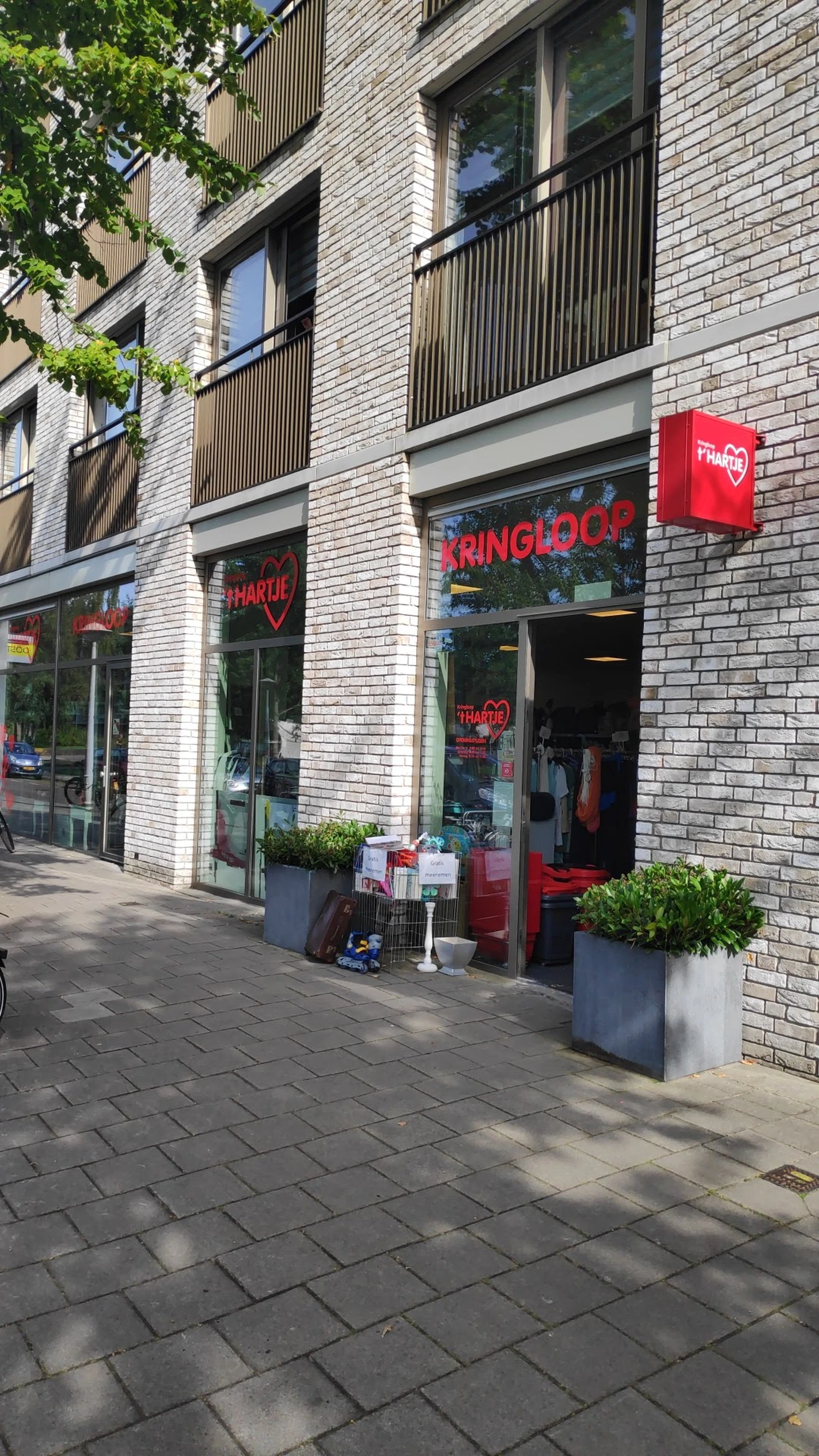 Gevel van kringloopwinkel met rode neonletters 'KRINGLOOP' en 'HARTJE', groene plantenbakken en open deur