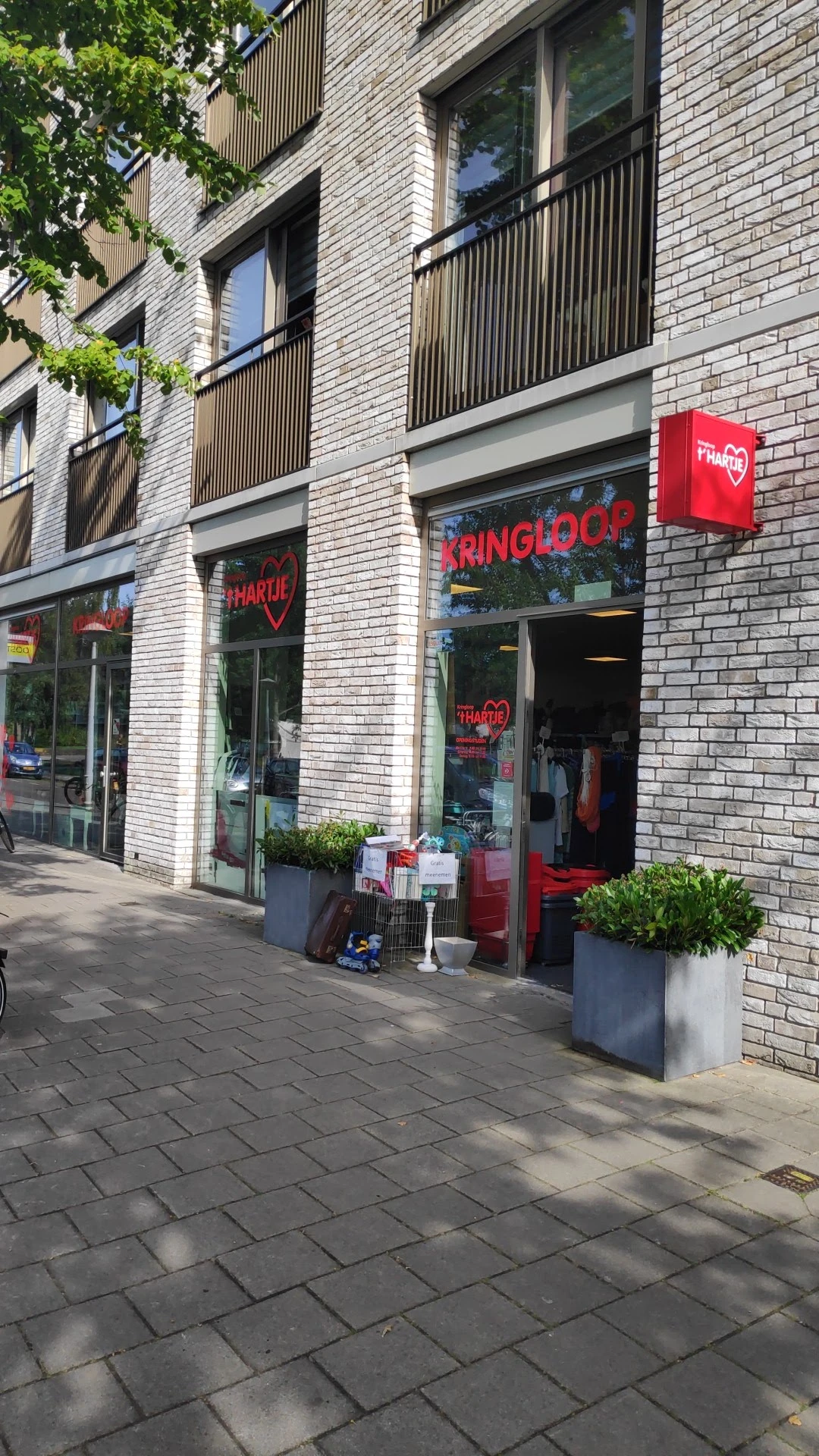 Gevel van kringloopwinkel met rode neonreclames en groene plantenbakken op straat