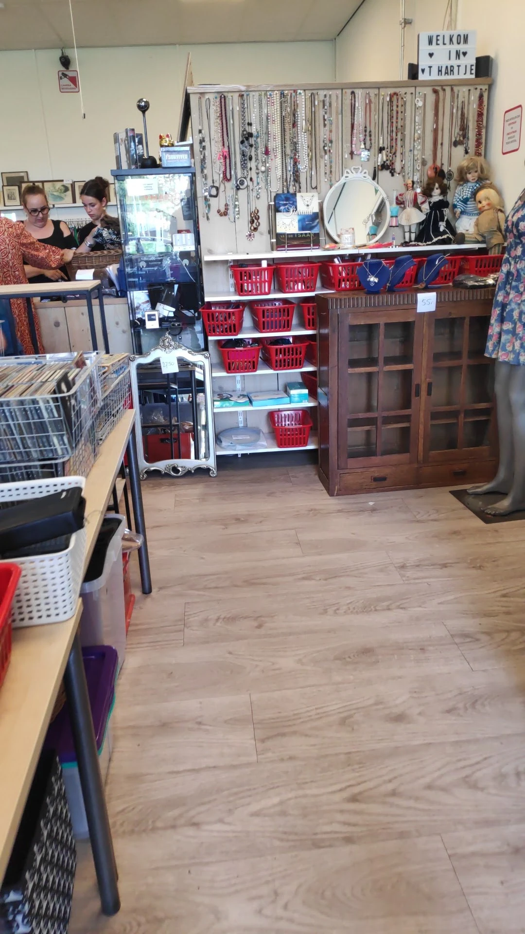 Winkelvloer met stellingen vol rode manden, houten kasten en diverse tweedehands spullen