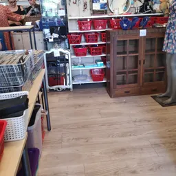 Winkelvloer met stellingen vol rode manden, houten kasten en diverse tweedehands spullen