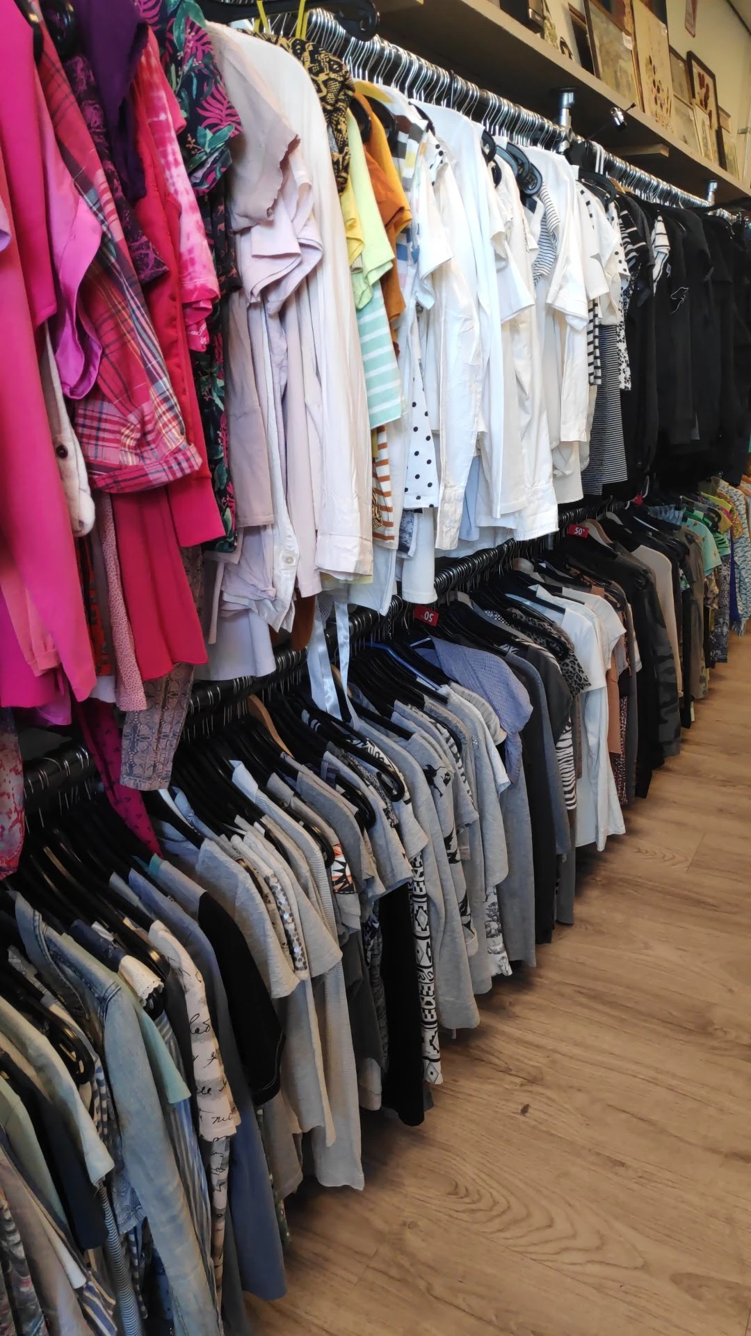 Rekken met tweedehands kleding op hangers, vooral broeken en tops in neutrale kleuren