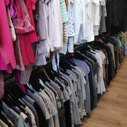 Rekken met tweedehands kleding op hangers, vooral broeken en tops in neutrale kleuren