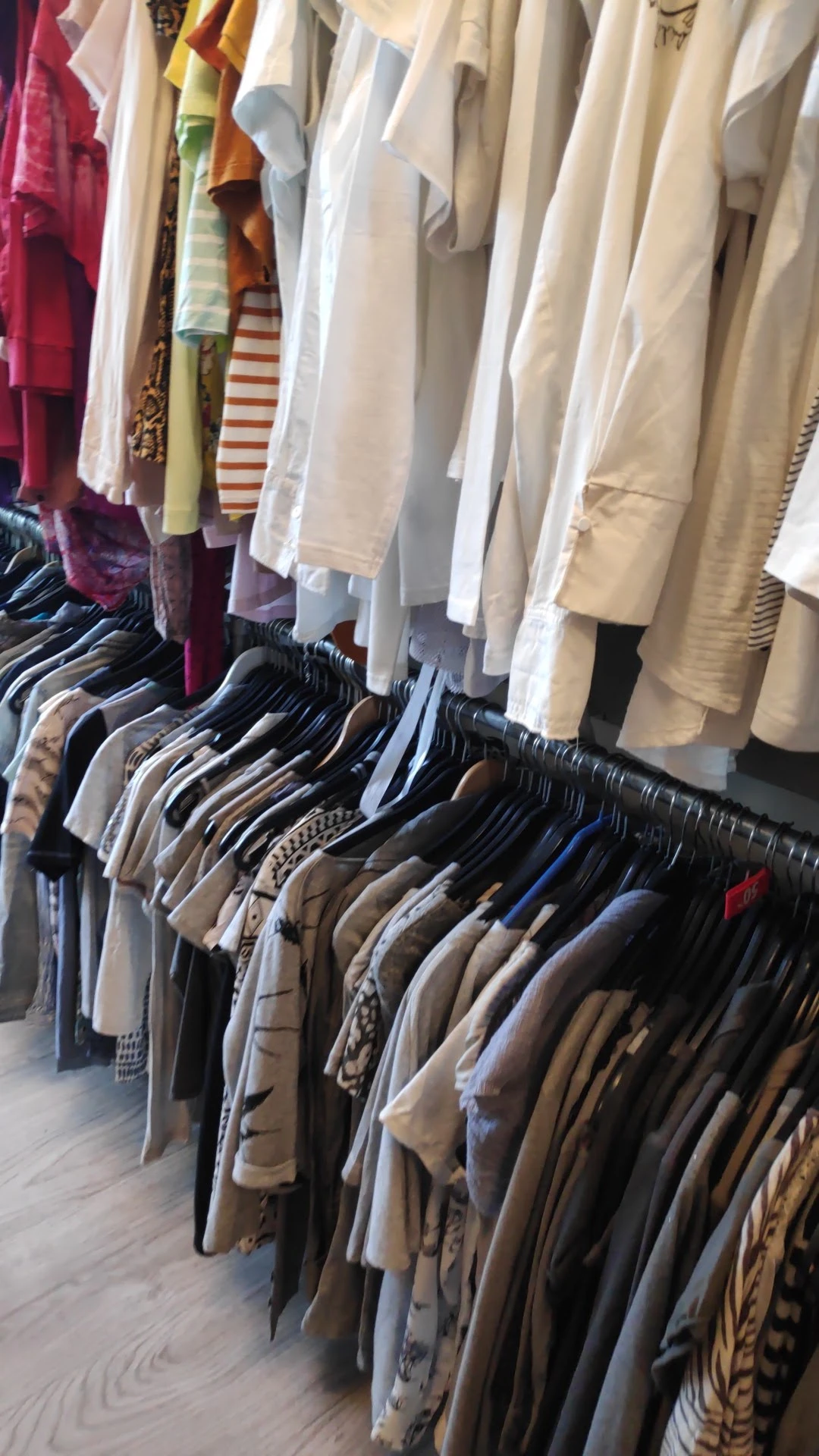 Rekken met tweedehands kleding op hangers, onder aan zichtbare overhemden en jasjes in neutrale tinten