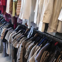 Rekken met tweedehands kleding op hangers, onder aan zichtbare overhemden en jasjes in neutrale tinten