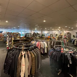 Overzicht van de winkelvloer met rekken vol tweedehands kleding, boekenkasten en merchandise onder fluorescente verlichting
