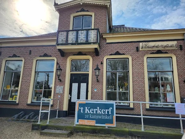 Gevel van kringloopwinkel met bakstenen muur, gele kozijnen, grote ramen en welkomstbord op de stoep