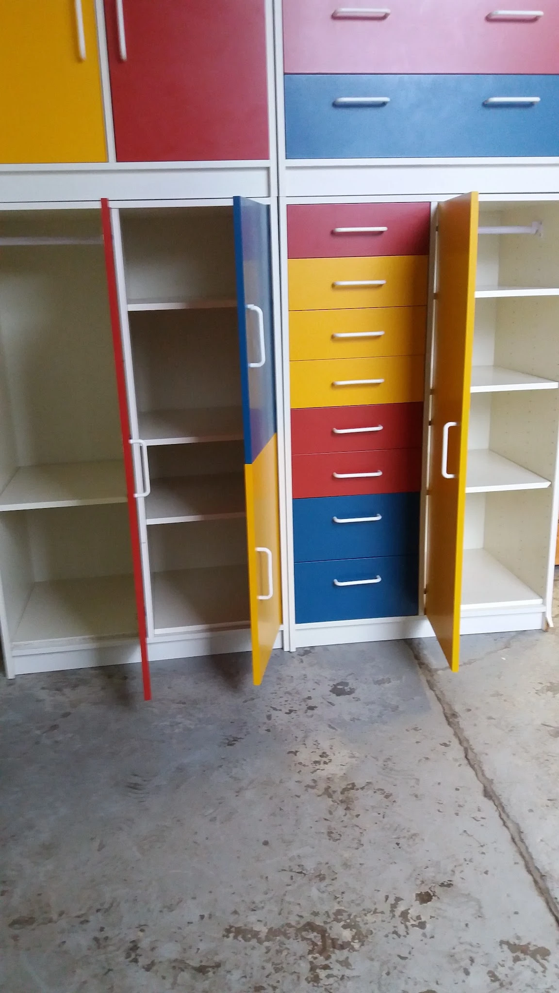 Gekleurde draaideurkast met laden in rood, geel en blauw naast open kastjes