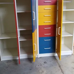 Gekleurde draaideurkast met laden in rood, geel en blauw naast open kastjes