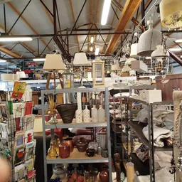 Ruim magazijn met stellingen vol huishoudartikelen, lampen, servies en decoraties onder houten balkenplafond