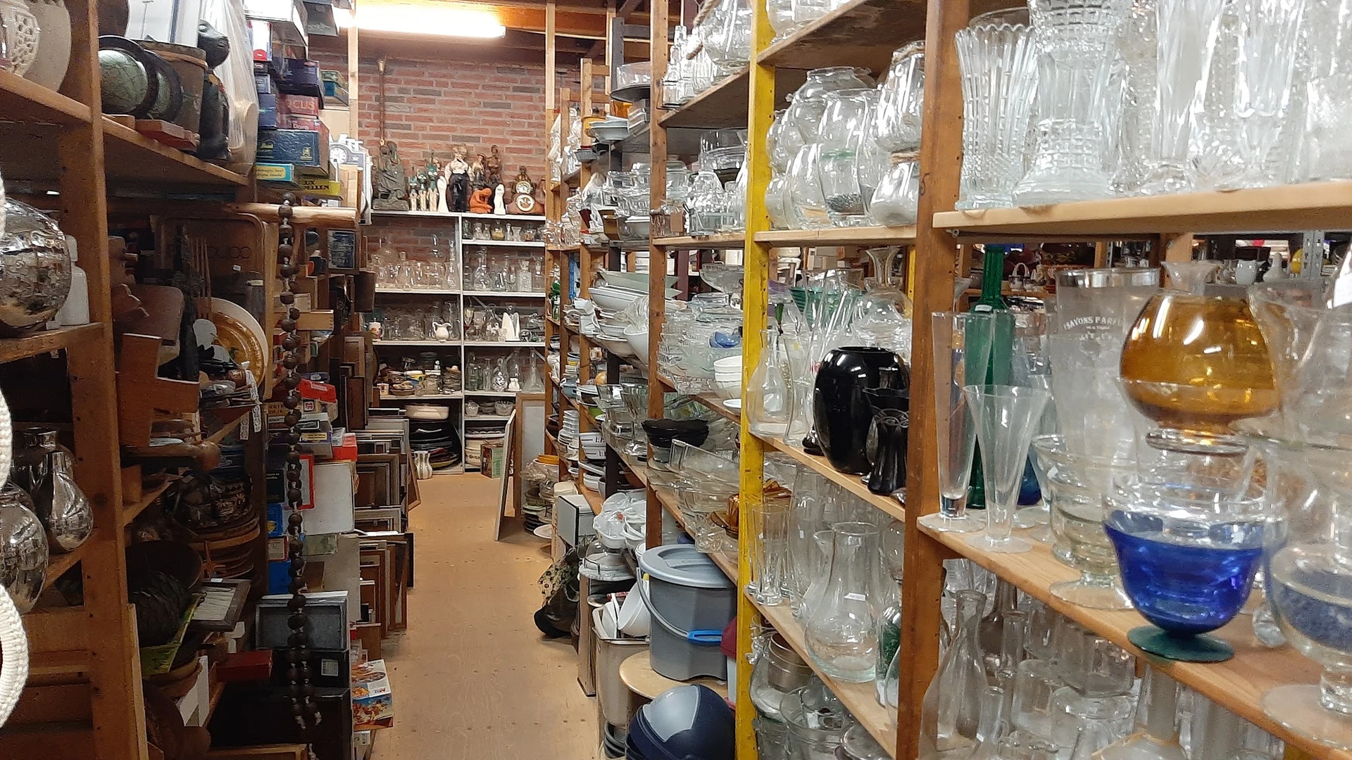 Houten stellingen met glazen potten, kruiken en flessenmagazijn in een kringloopwinkel