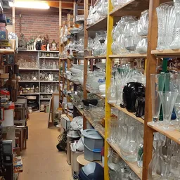 Houten stellingen met glazen potten, kruiken en flessenmagazijn in een kringloopwinkel