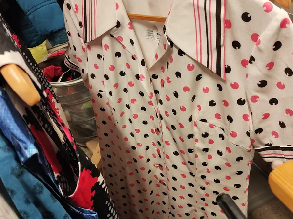Uitgestalde damesblouses met roze en zwarte stippenprint op hangers in de winkel