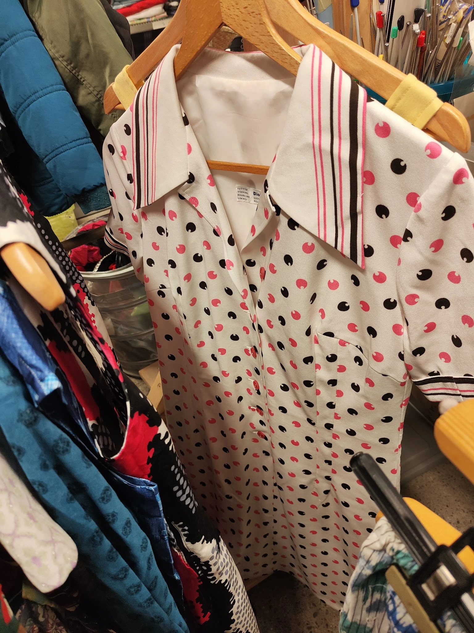 Uitgestalde damesblouses met roze en zwarte stippenprint op hangers in de winkel