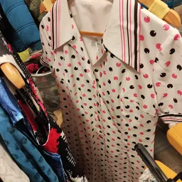 Uitgestalde damesblouses met roze en zwarte stippenprint op hangers in de winkel