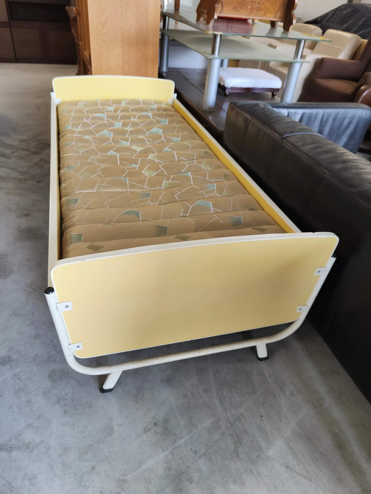 Geel kinderbedje met wit frame en matras met patroon