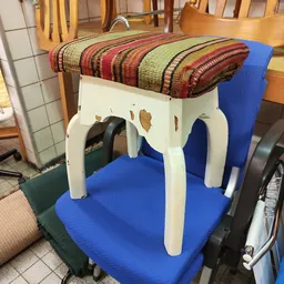 Witte kruk of tafel met gestreepte stofkussenzitting, staand op blauwe ondergrond