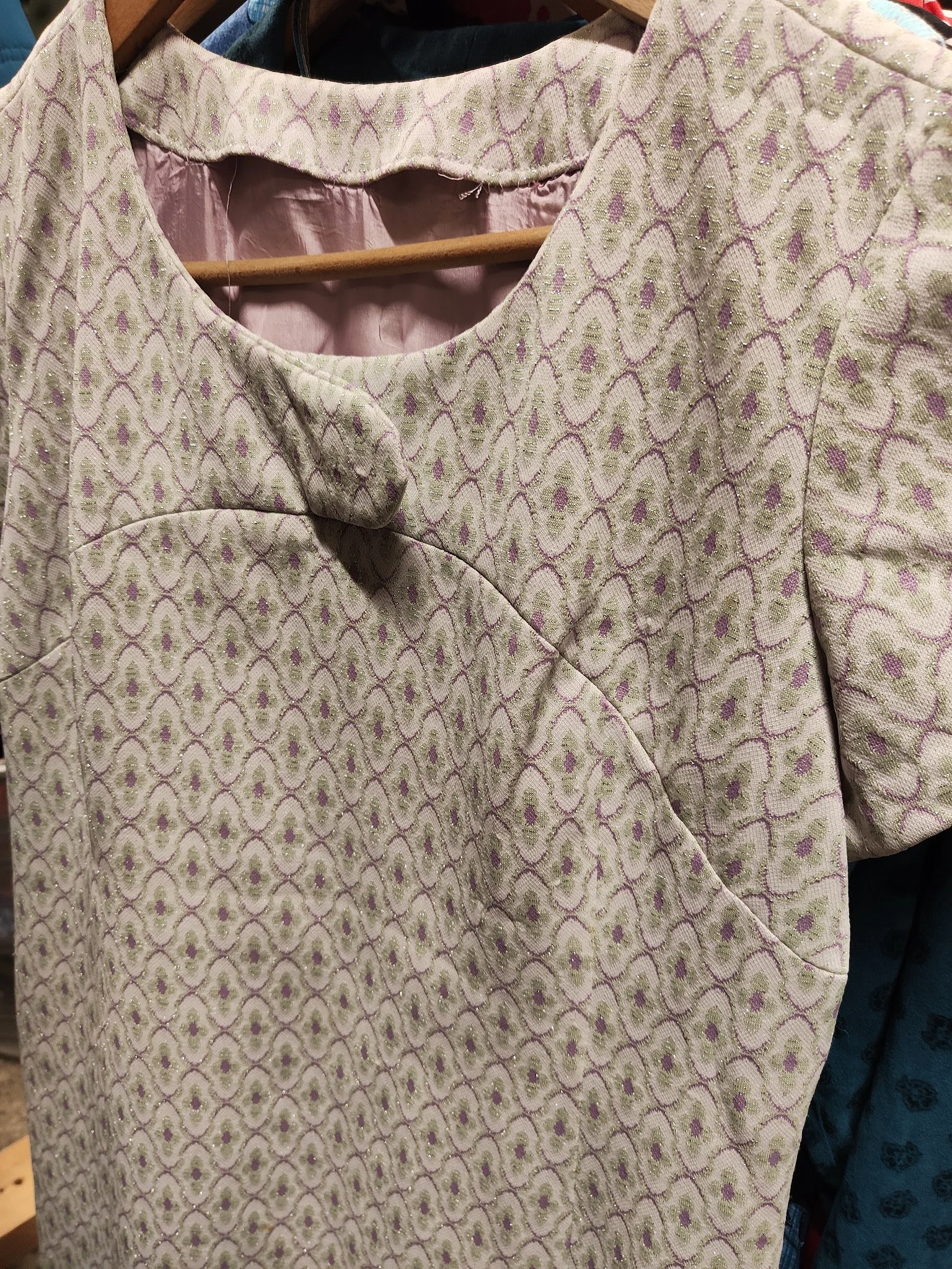 Close-up van een beige knitwear kledingstuk met paars geometrisch patroon en zichtbare draad