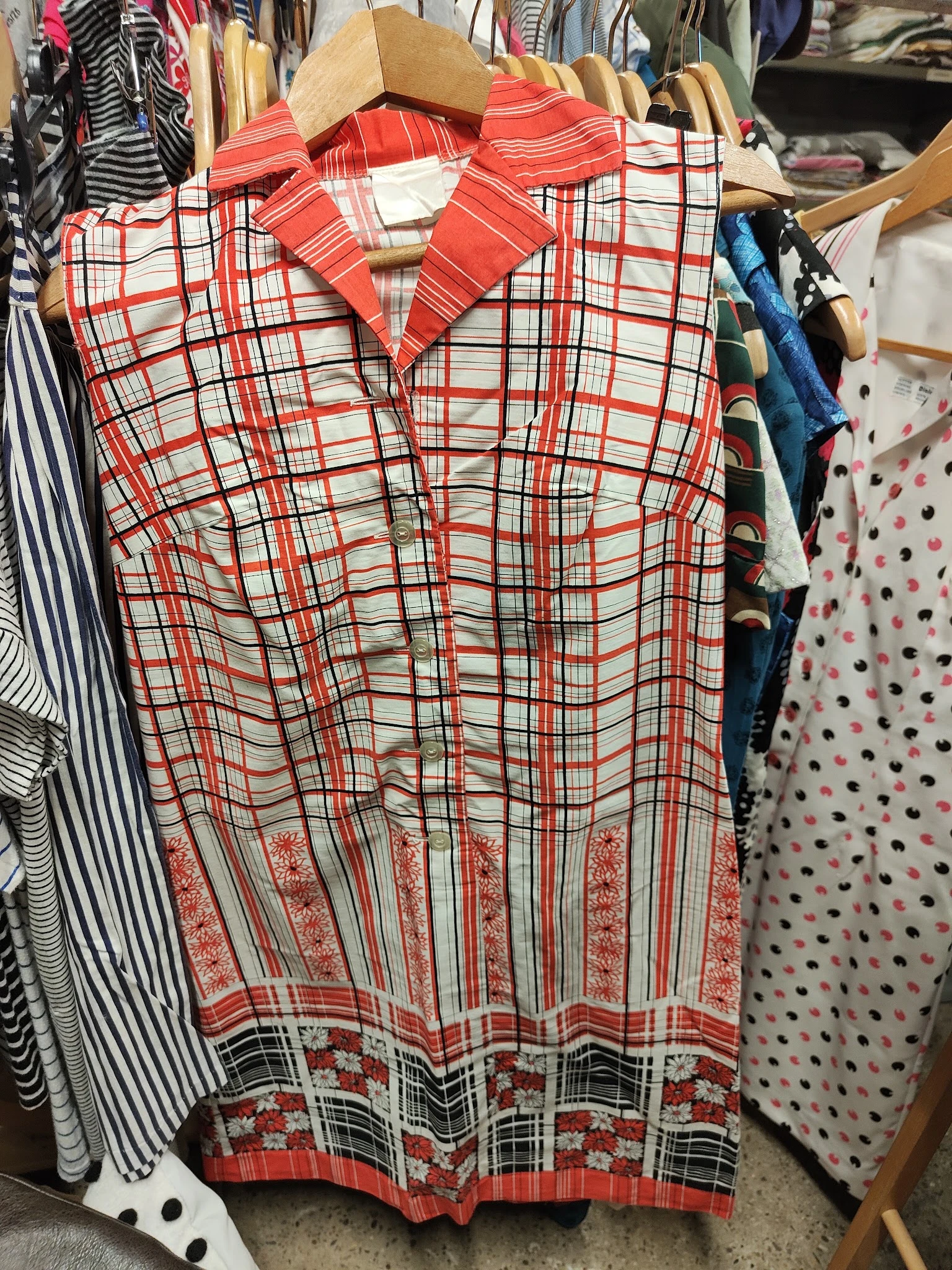 Rekken met tweedehands kleding, waaronder een rood geruit hemd op hangers in een kringloopwinkel.