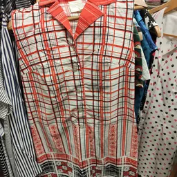 Rekken met tweedehands kleding, waaronder een rood geruit hemd op hangers in een kringloopwinkel.