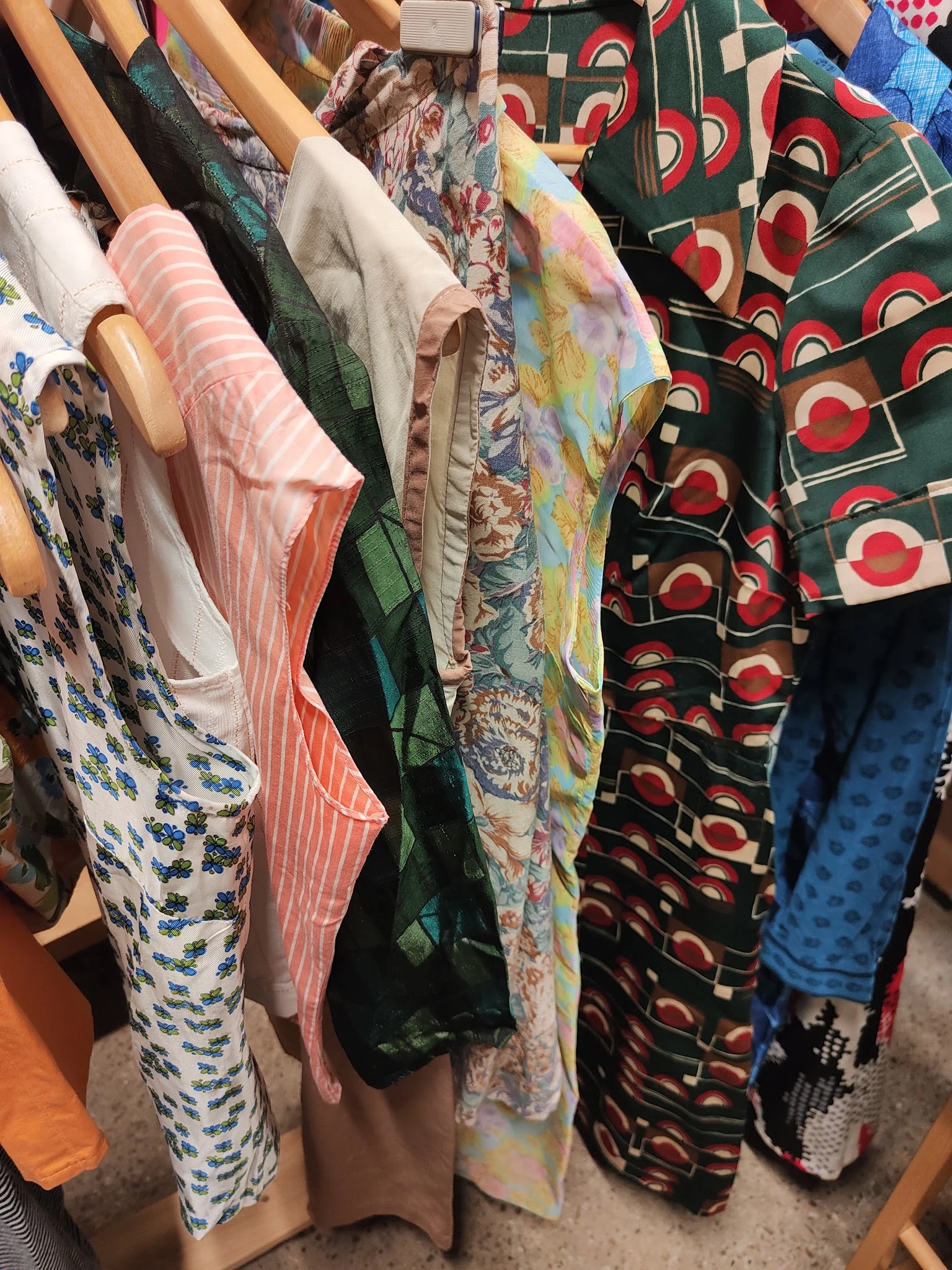 Rekken met tweedehands kleding in verschillende kleuren en patronen, waaronder roze gestreepte en rode stoffen