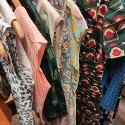 Rekken met tweedehands kleding in verschillende kleuren en patronen, waaronder roze gestreepte en rode stoffen