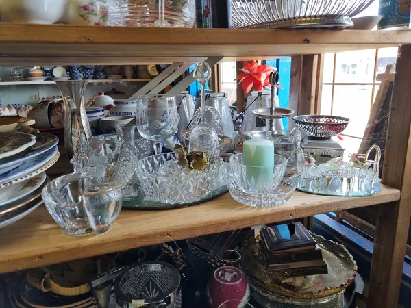 Houten plank met glazen schalen, karaffen en serviesgoed in een kringloopwinkel