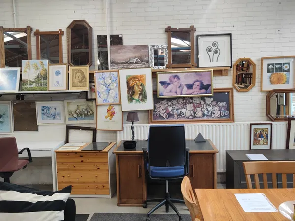 Werkplek met bureau, stoel en muur vol ingelijste foto's, schilderijen en spiegels