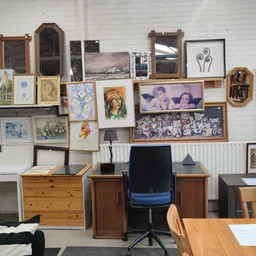 Werkplek met bureau, stoel en muur vol ingelijste foto's, schilderijen en spiegels