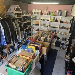 Winkelinterieur met kledingrekken aan de linkerkant, boekenkasten in het midden en dozen met tweedehands spullen op de vloer