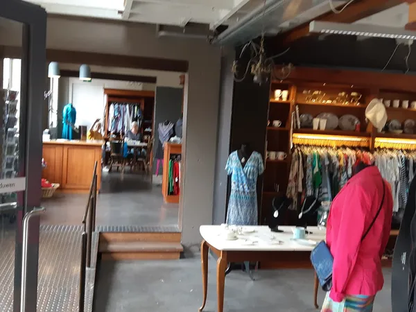 Winkelinterieur met kledingrekken, houten tafels en goederen uitgestald