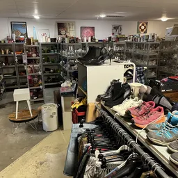 Winkelinterieur met stellingen vol spullen, schoenen op tafels en kleding in het zicht