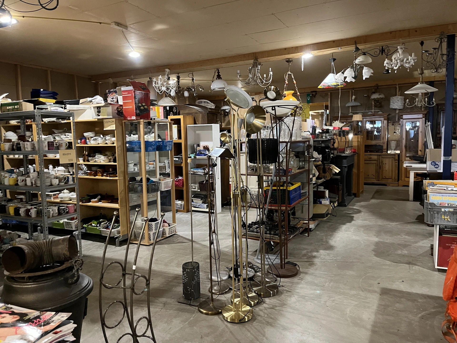 Winkelvloer van kringloopwinkel met stellingen, hangers met diverse spullen en huishoudelijke artikelen