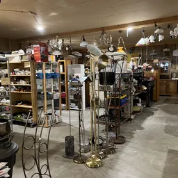 Winkelvloer van kringloopwinkel met stellingen, hangers met diverse spullen en huishoudelijke artikelen