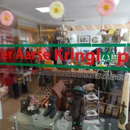 Winkelraam met groene winkelnaambord en decoratieve bloemen, uitzicht op winkelvloer met stellingen en spullen