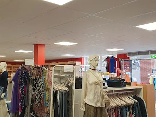 Rekken met tweedehands kleding, inclusief jurken en broeken, met een etalagepop in beige kleding