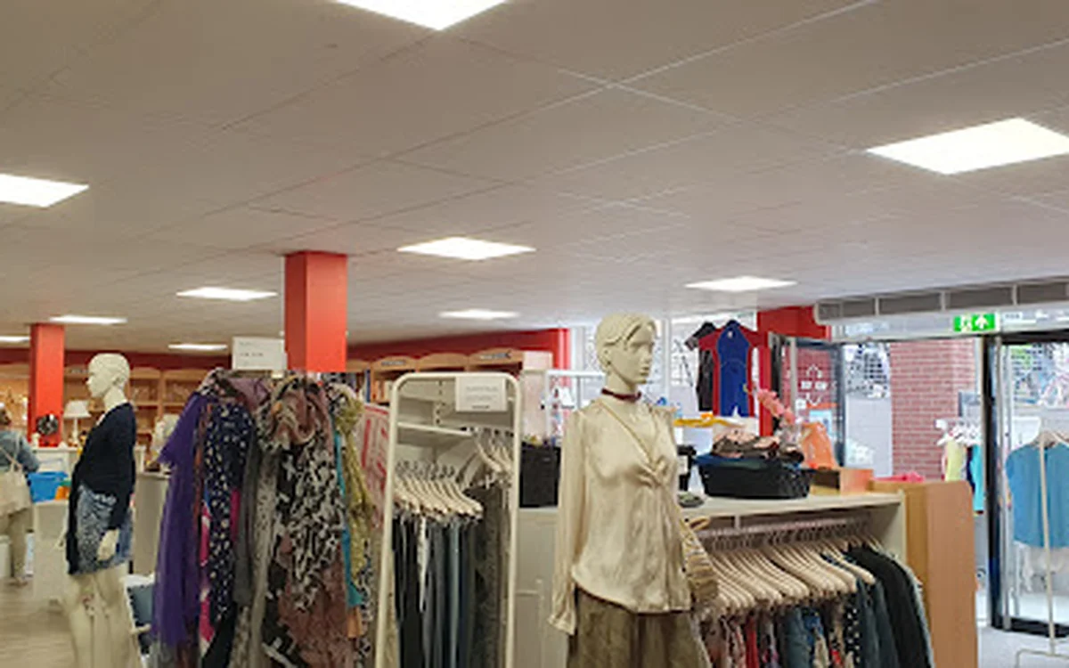 Rekken met tweedehands kleding, inclusief jurken en broeken, met een etalagepop in beige kleding