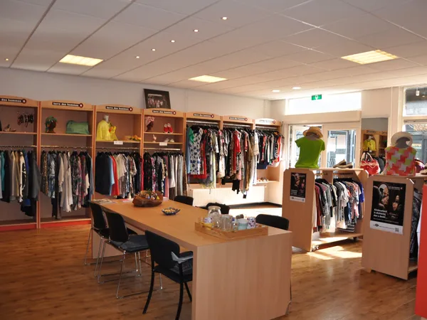 Winkelvloer met kledingrekken, houten toonbank en houten kasten met tweedehands kleding