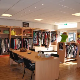 Winkelvloer met kledingrekken, houten toonbank en houten kasten met tweedehands kleding