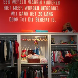 Kinderkleding uitgestald in open kasten met rood inspiratiebordje aan de muur