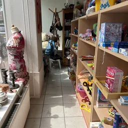 Gangarrangement in kringloopwinkel met stellingen vol spullen, speelgoed en huishoudartikelen aan beide zijden