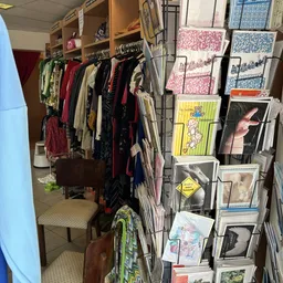 Rekken met tweedehands kleding en muurrek met uitgestalde boeken, posters en andere artikelen