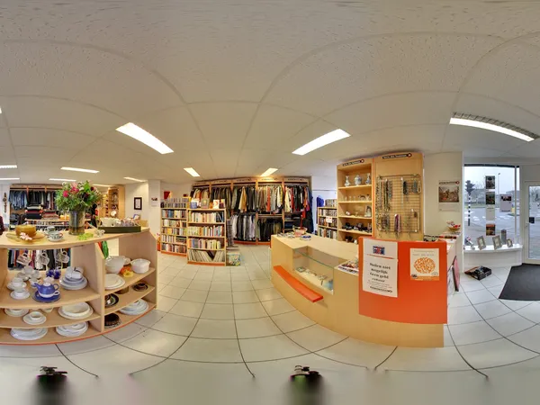 Panoramisch overzicht van kringloopwinkelruimte met kledingrekken, boekenkasten, serviesgoed en meubelstukken